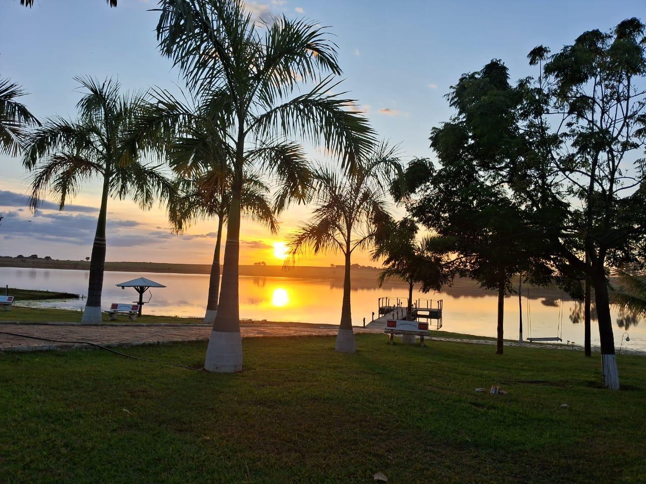 Pôr do Sol cinematográfico sobre o lago na Chácara Vitória com pier e coqueiros