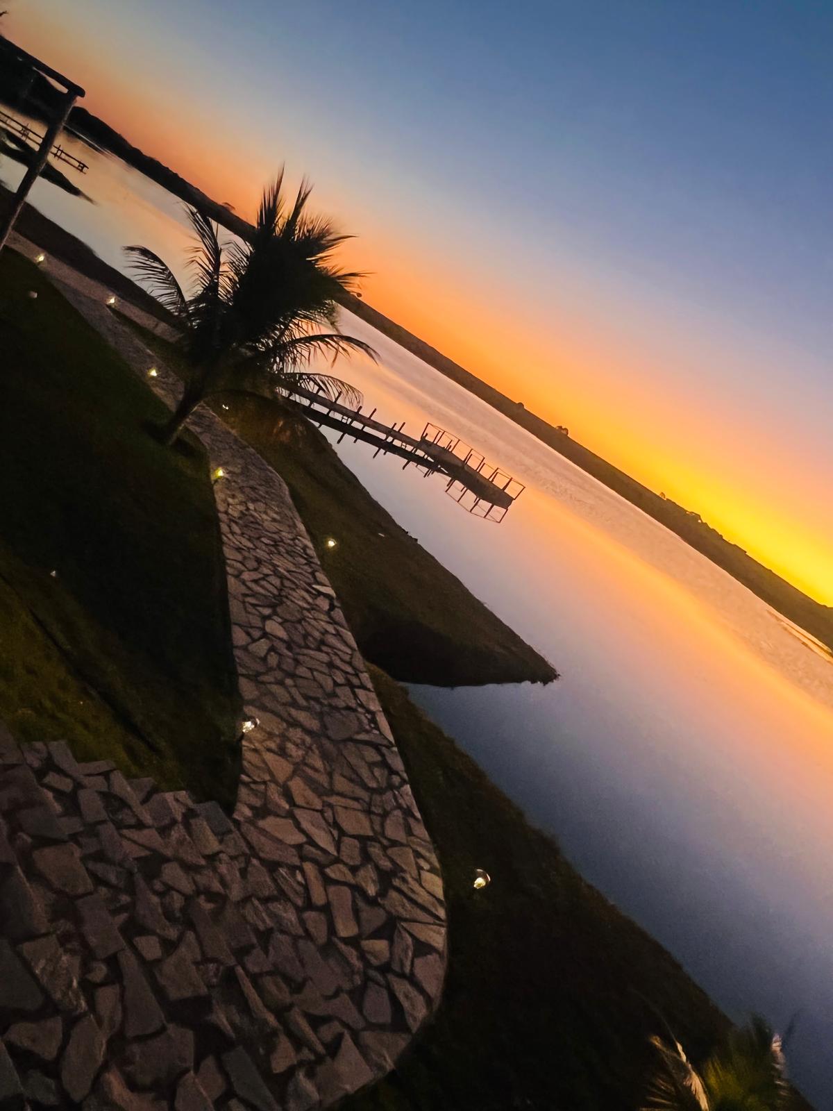 Caminho de pedra portuguesa iluminado contornando a represa ao entardecer